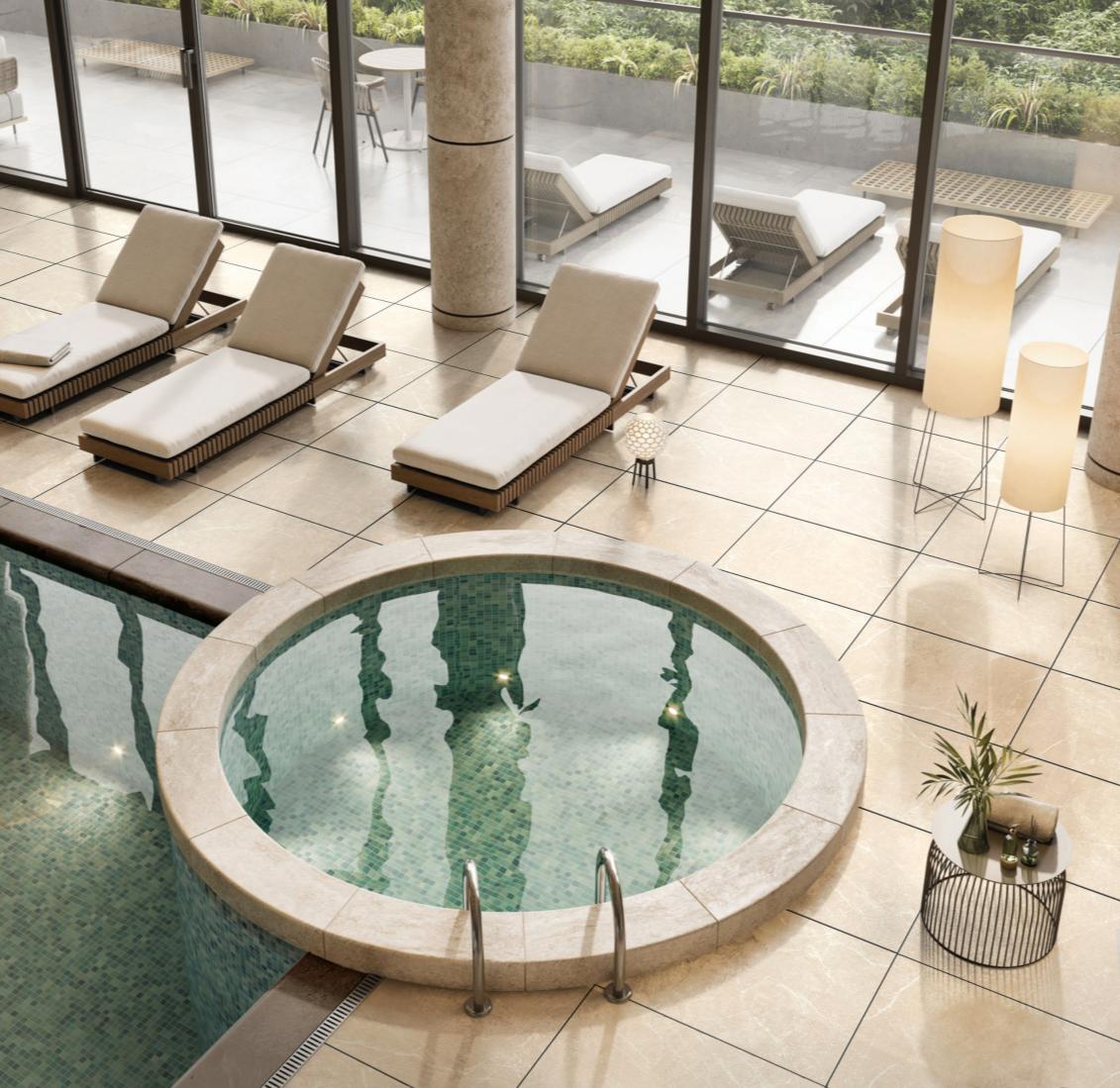 Modern indoor pool area with a round hot tub, beige lounge chairs, and floor lamps near large glass windows.