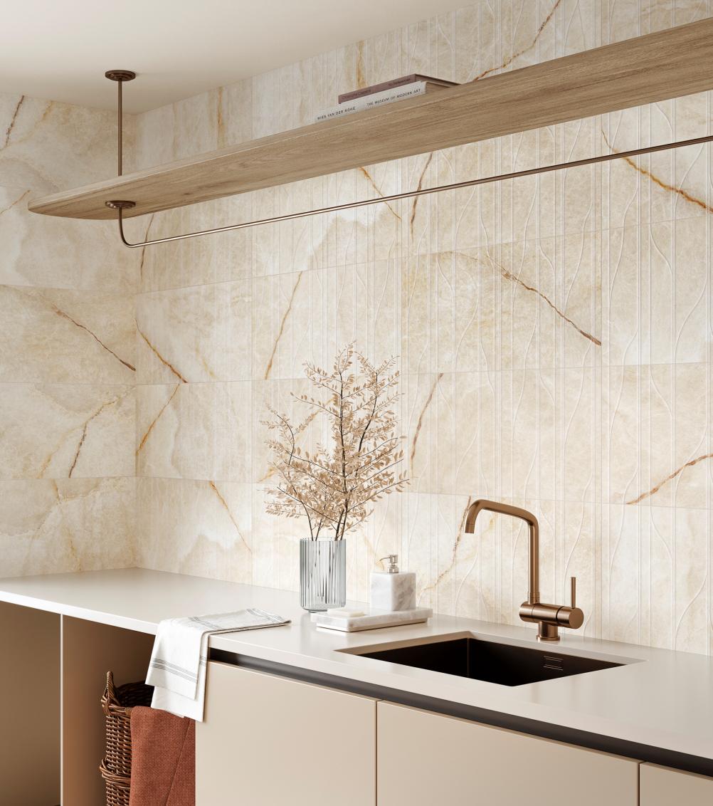 Modern kitchen countertop with beige cabinets, a black sink with a bronze faucet, marble soap dispenser, dried branches in a glass vase, and a wooden floating shelf above.