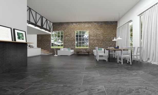 Modern living and dining area with gray stone tile floor, exposed brick wall, white furniture, and large windows with curtains.