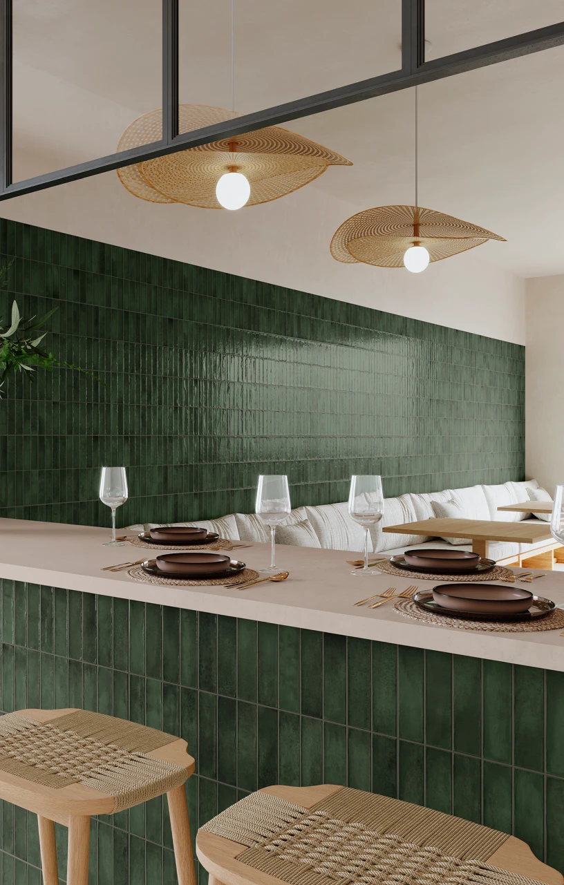 Modern dining area with green tiled walls and counter, wicker pendant lights, wooden stools with woven seats, and a white cushioned bench.