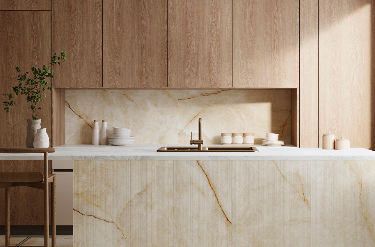 Modern kitchen with beige marble island, wood cabinets, brass faucet, and decorative ceramics on the counter.
