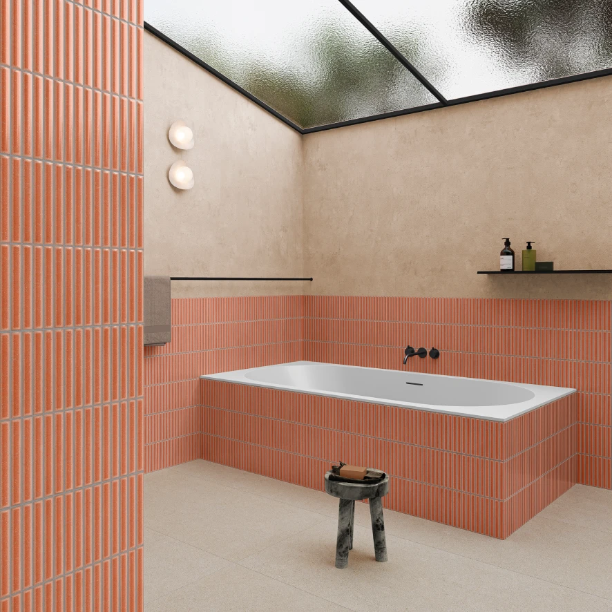 Modern bathroom with a rectangular bathtub surrounded by vertical orange tiles and beige walls, featuring a frosted glass ceiling and a small black stool with bath items.
