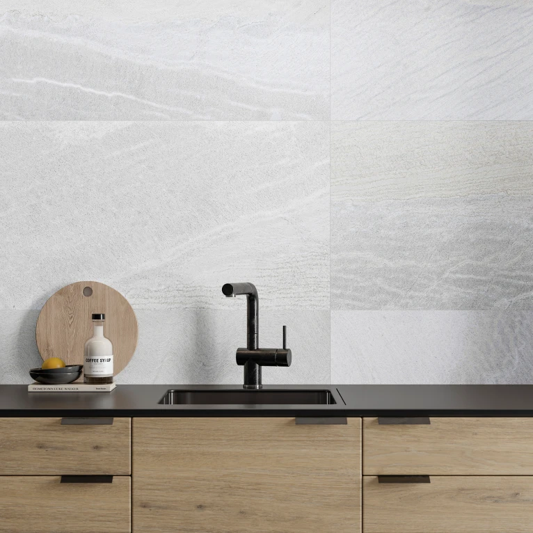 Modern kitchen sink with black faucet set against a light gray tiled backsplash and light wood cabinetry.