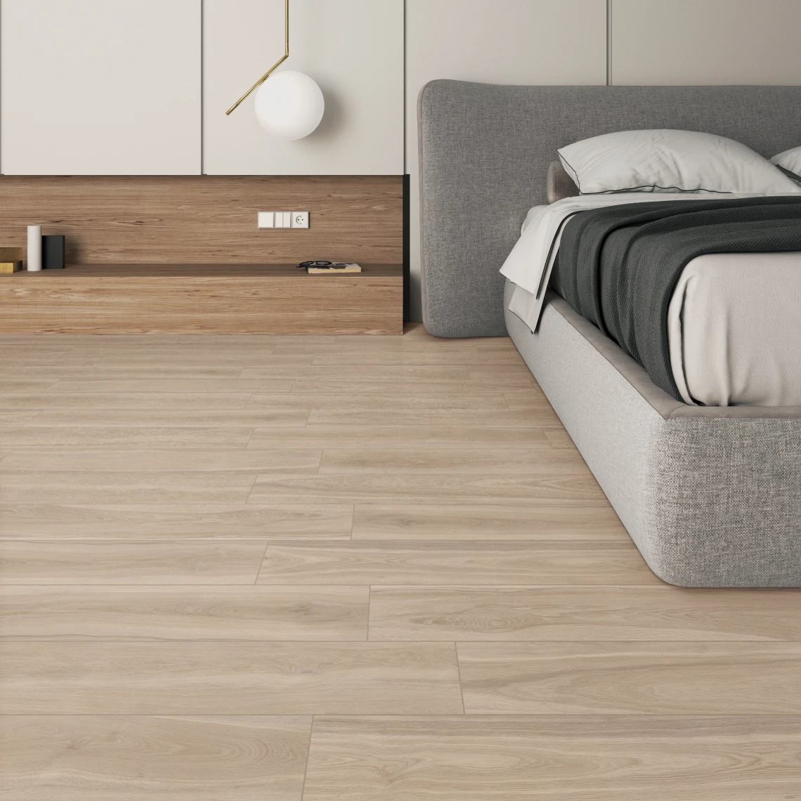 Minimalist bedroom corner with a gray upholstered bed, white and gray bedding, light wood flooring, and a low wood shelf with books and decorative objects.