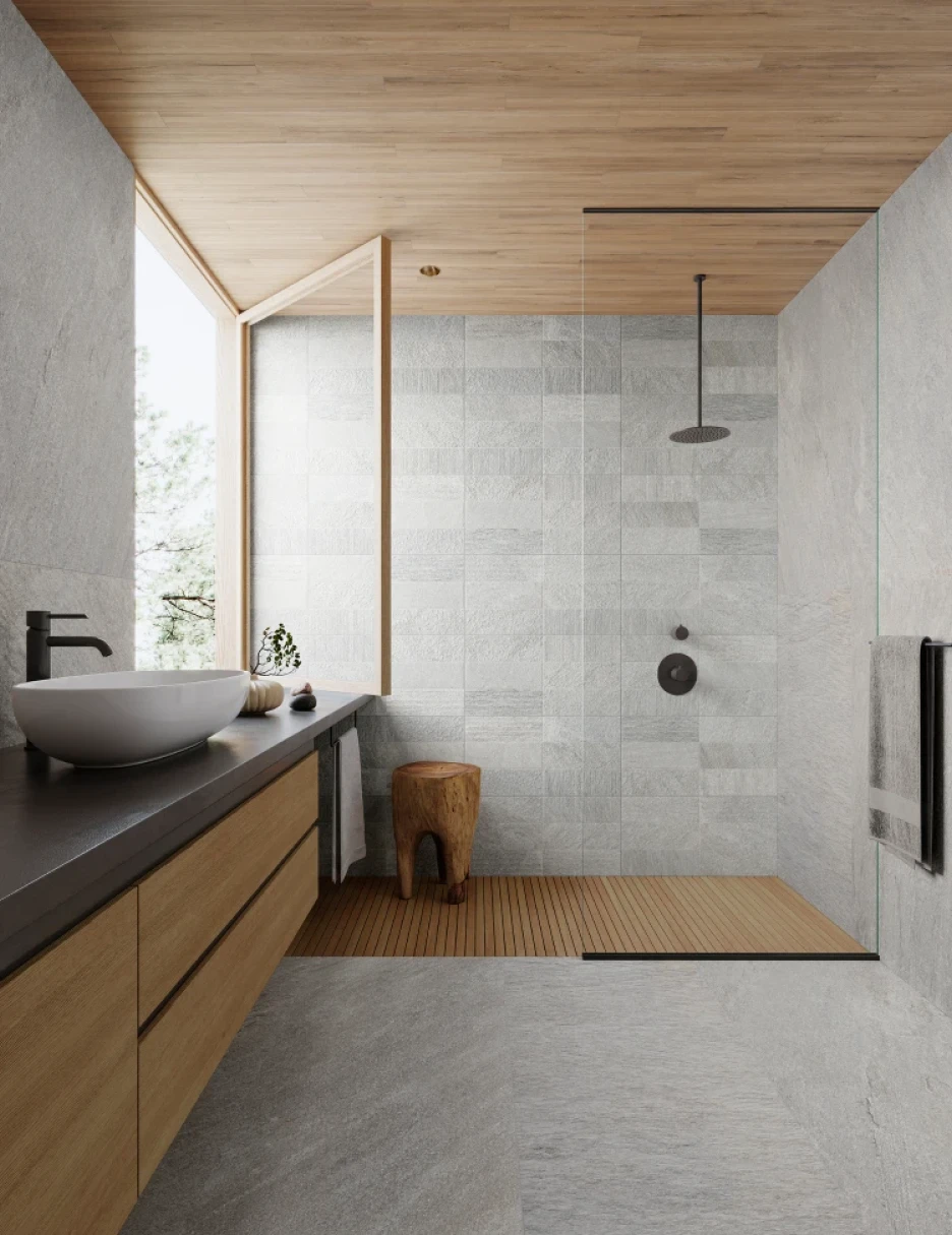 Modern bathroom with gray stone tiles, wooden ceiling, open window, wooden stool, black rain shower, and countertop sink with black faucet.