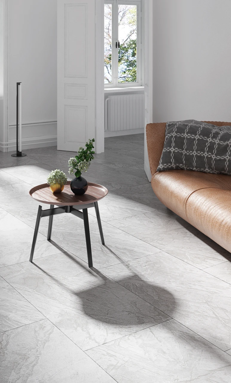 Modern living room corner with a brown leather sofa, a gray patterned cushion, a round wooden side table with two small vases holding green plants, and a white door opening to a window with a radiator beneath.