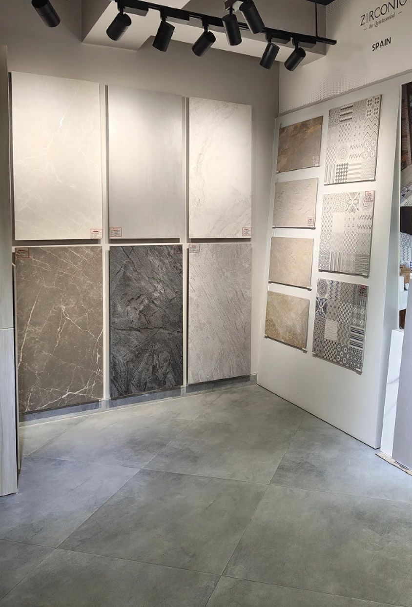 Showroom wall displaying large rectangular stone and tile samples in various neutral colors and patterns under ceiling spotlights.