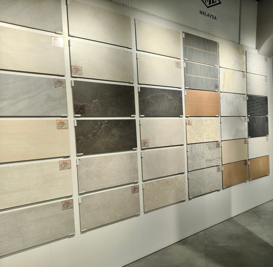 Display wall of various rectangular ceramic tiles in neutral colors and textures at a showroom.