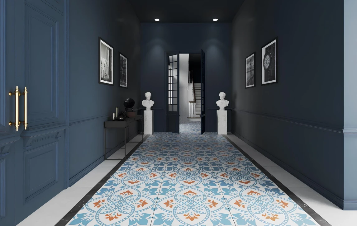 Dark blue hallway with patterned blue and orange tile floor, white bust statues on pedestals, black and white framed pictures on walls, and double doors opening to a staircase.