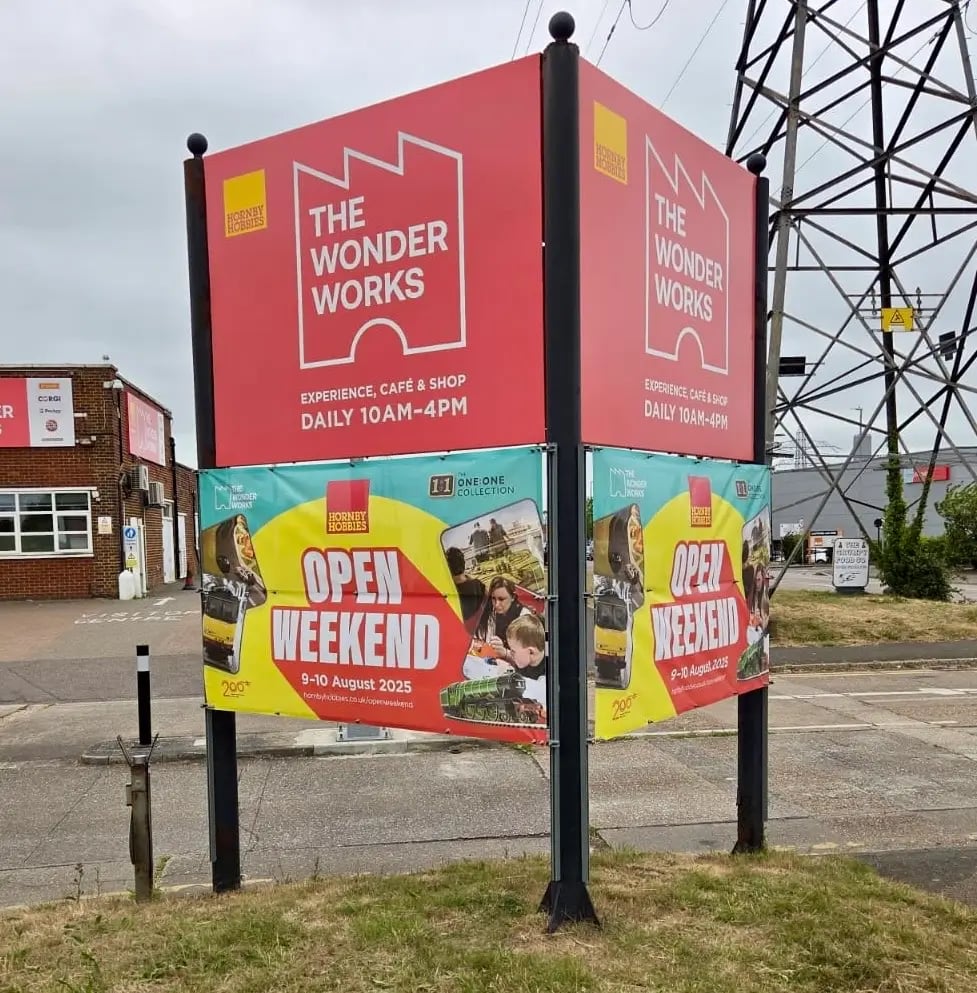 Two-sided outdoor sign for The Wonder Works by Hornby Hobbies showing daily hours and Open Weekend event 9-10 August 2025 with images of model trains and people.