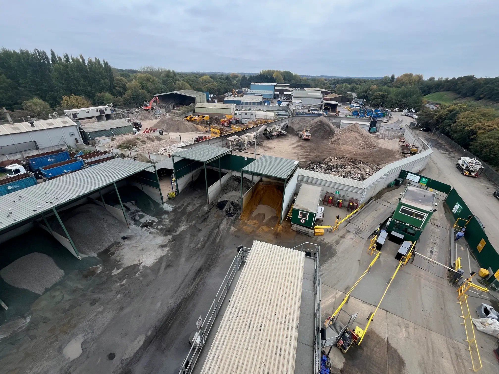 Aerial view of an industrial construction site with storage bins holding gravel and sand, heavy machinery, and dirt piles.