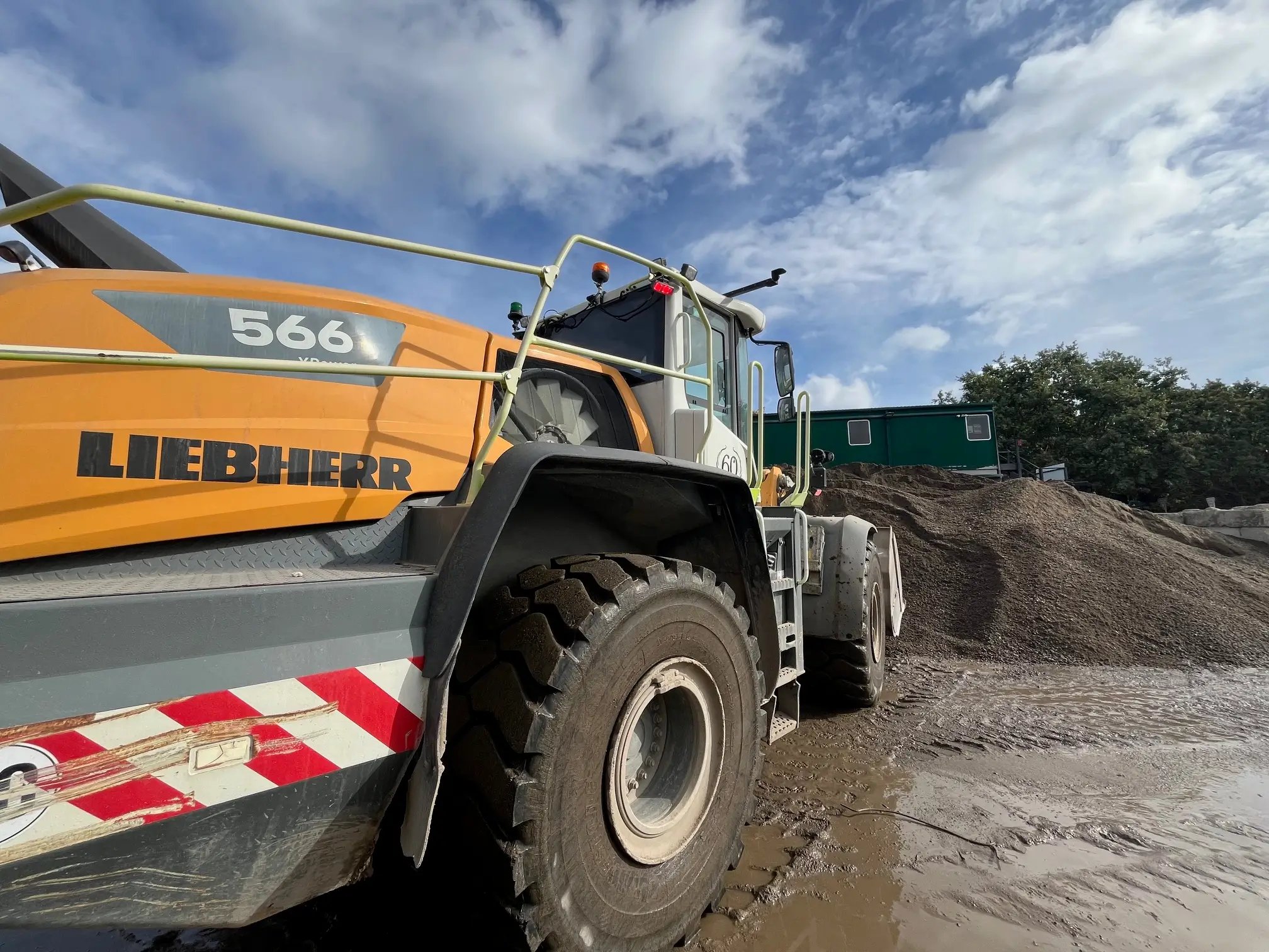 Close-up of a large Liebherr construction vehicle parked near a pile of gravel under a partly cloudy sky.