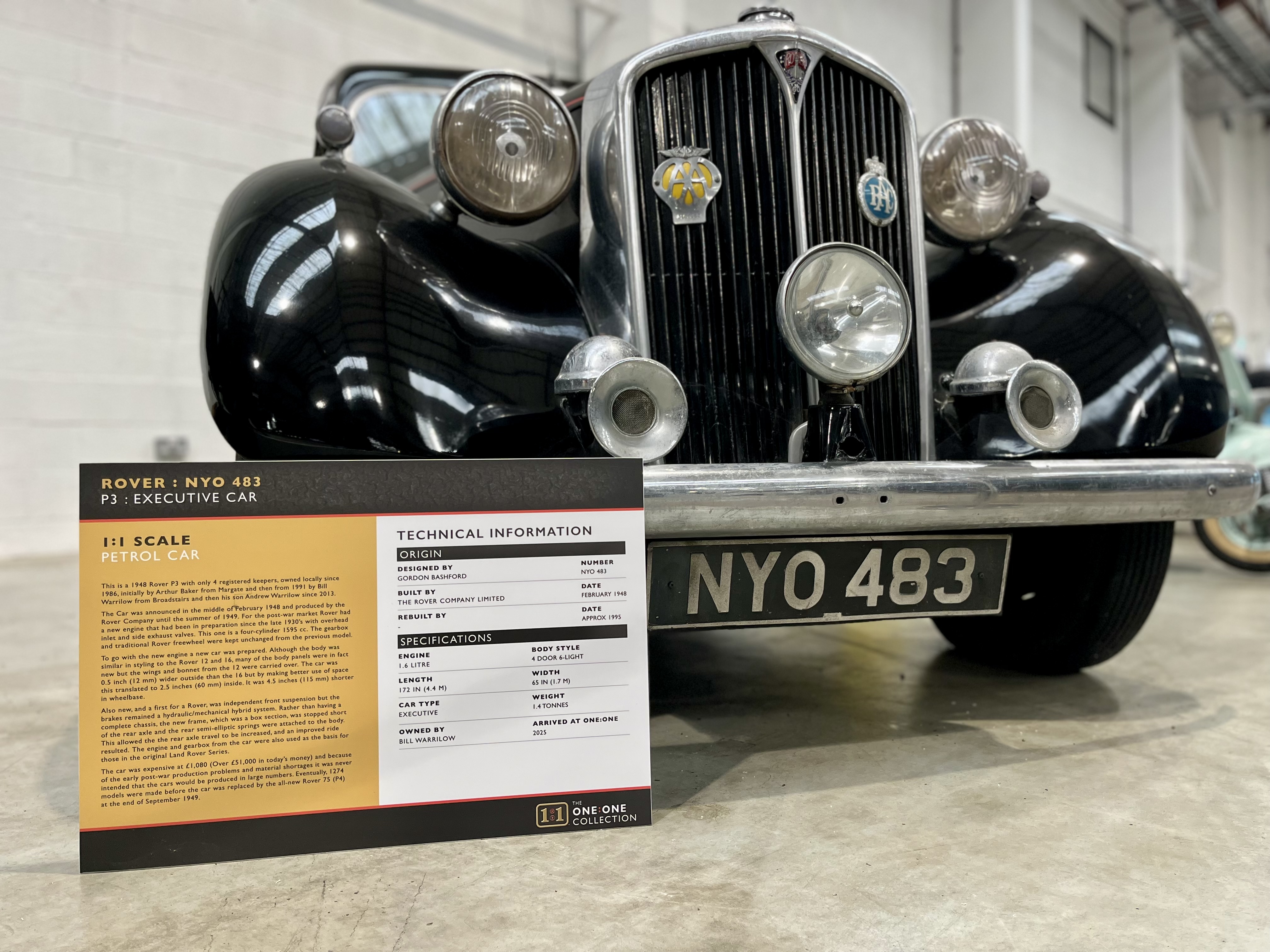 Front view of a black 1948 Rover P3 car with license plate NYO 483 and an informational sign in front.