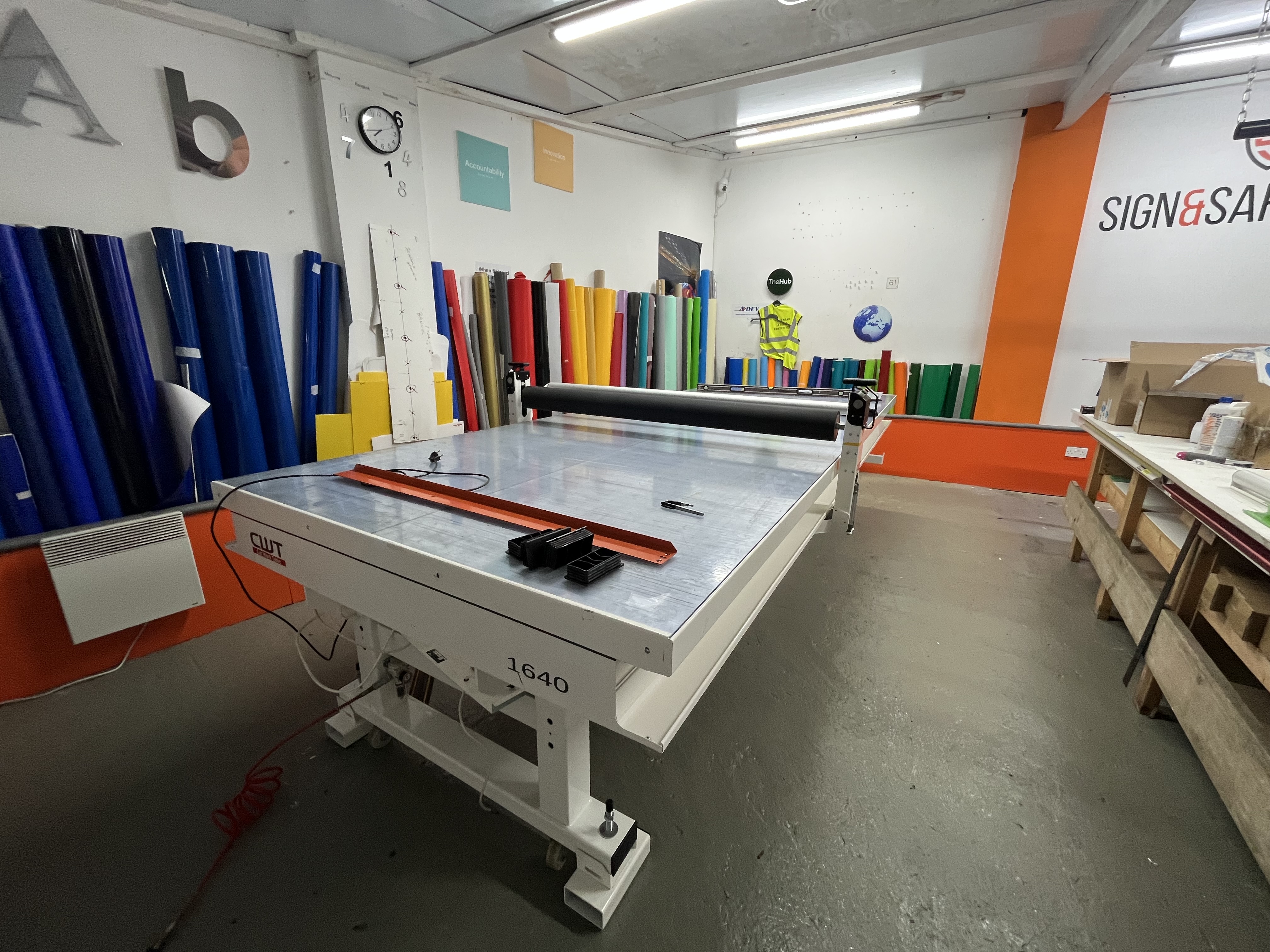 Large cutting table surrounded by rolls of colored vinyl in a sign-making workshop.