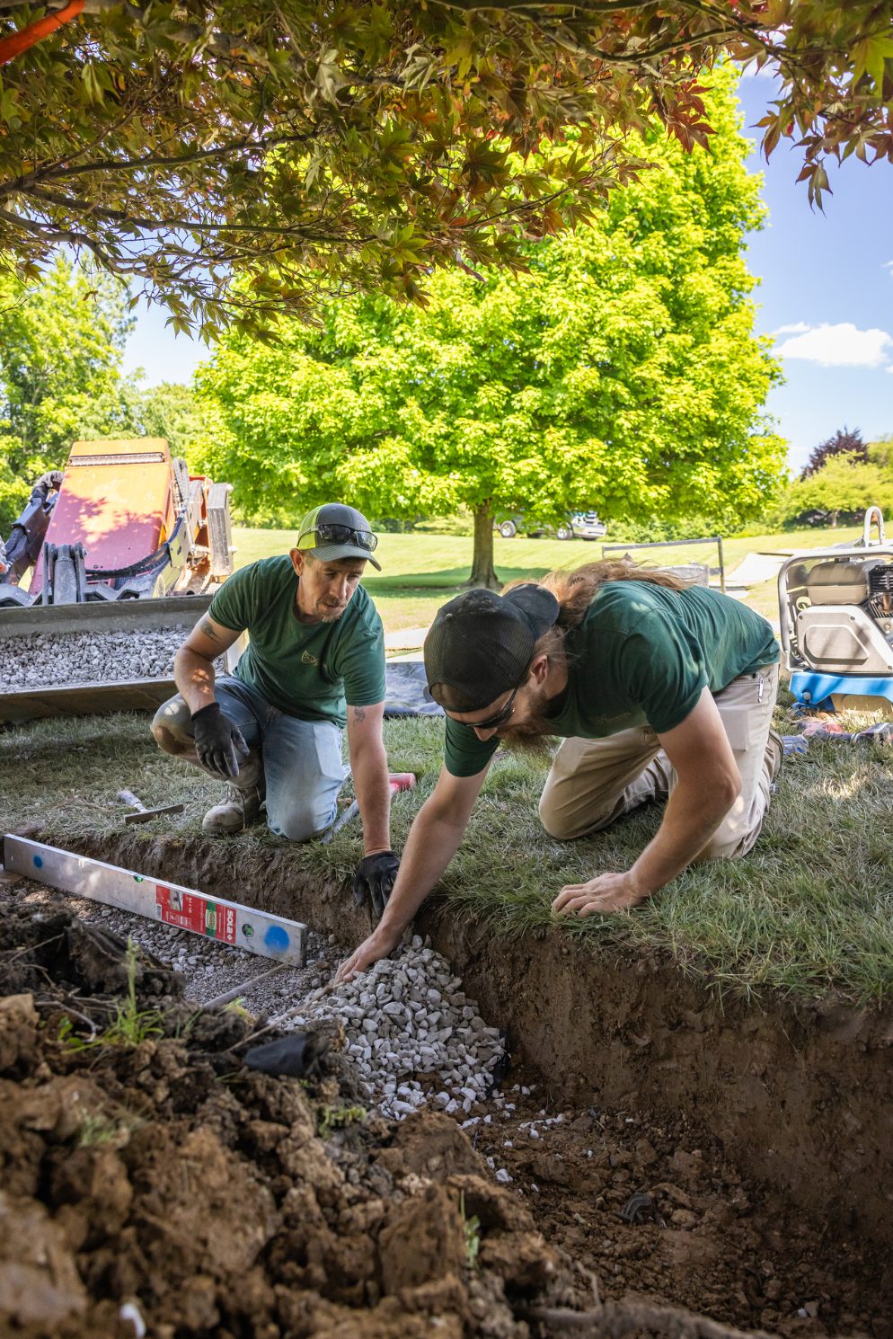 Two crew members setting a gravel base by hand on site