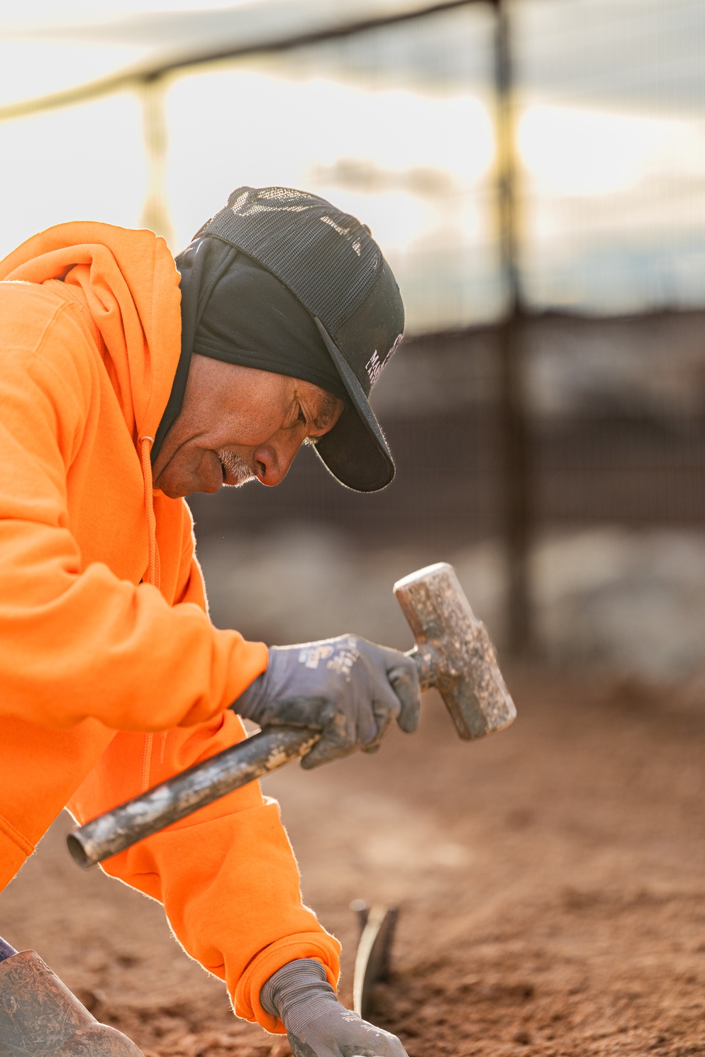 Crew member driving a stake with a sledgehammer at golden hour