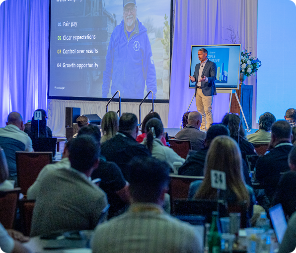 Man in blue shirt speaking to a seated audience at a LeanScaper Intensive event.