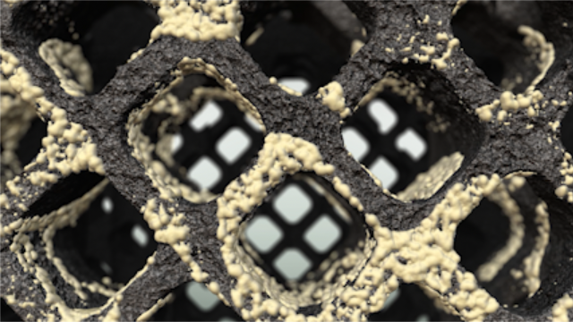 Close-up of a porous, lattice-like structure with a rough yellowish coating and square openings.