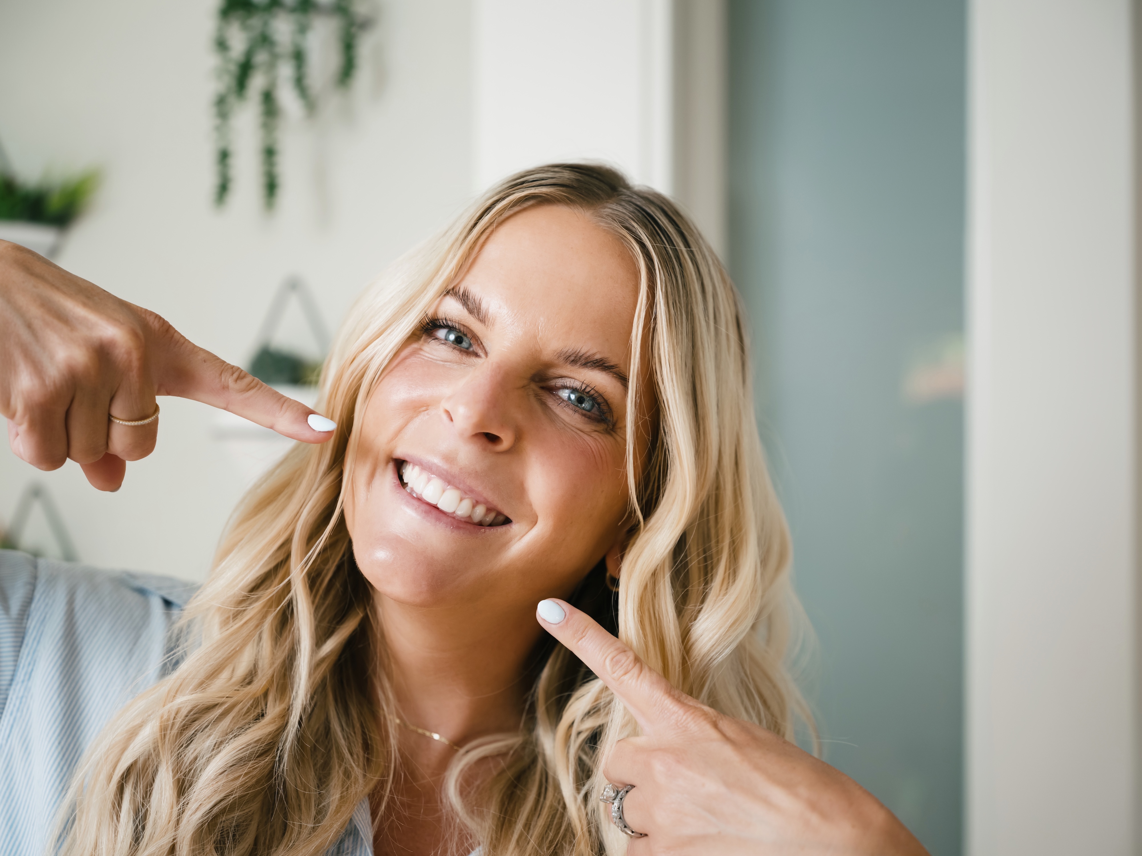 A woman is smiling and pointing to her smile with both hands.