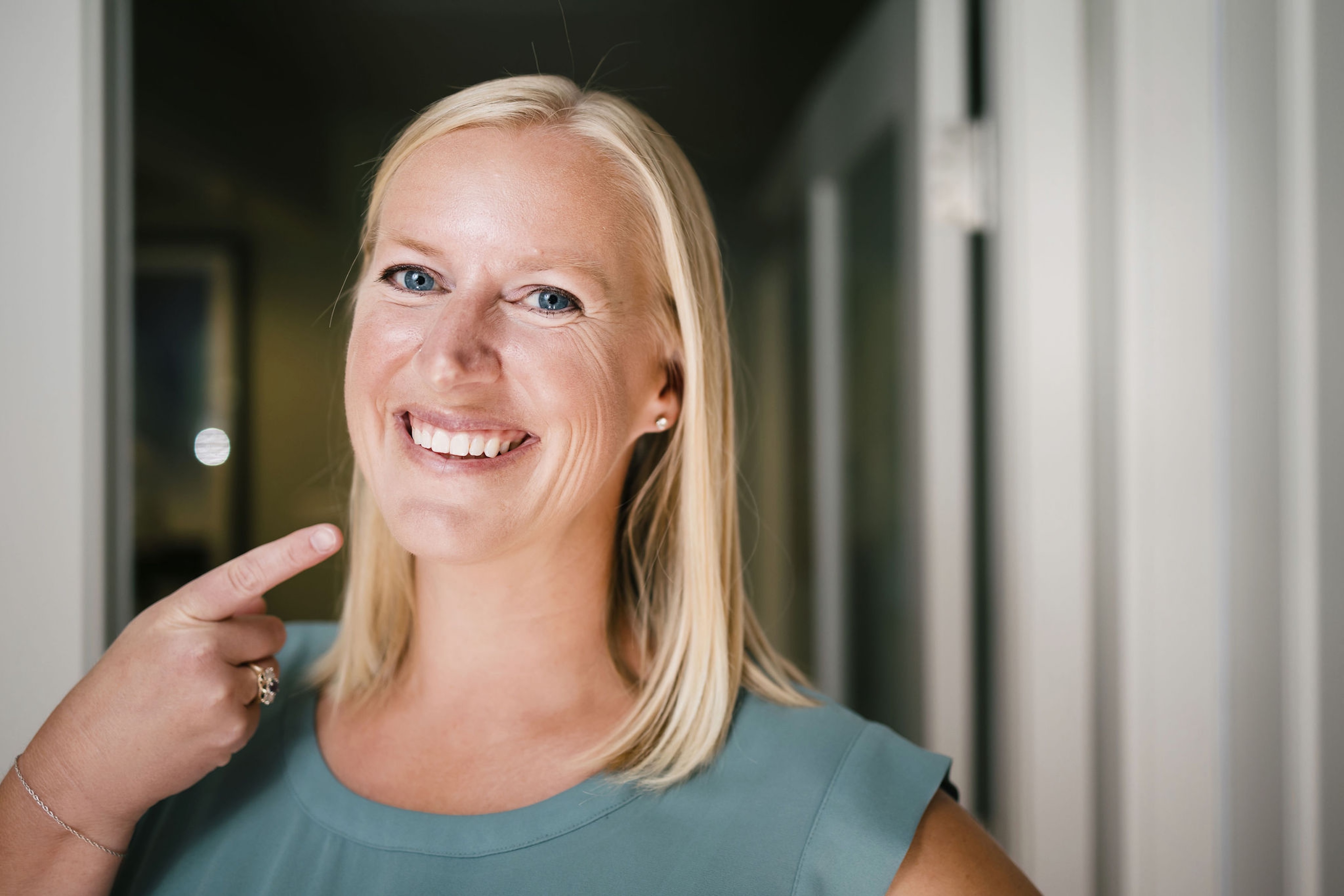 A woman is smiling and pointing to her smile with one hand.
