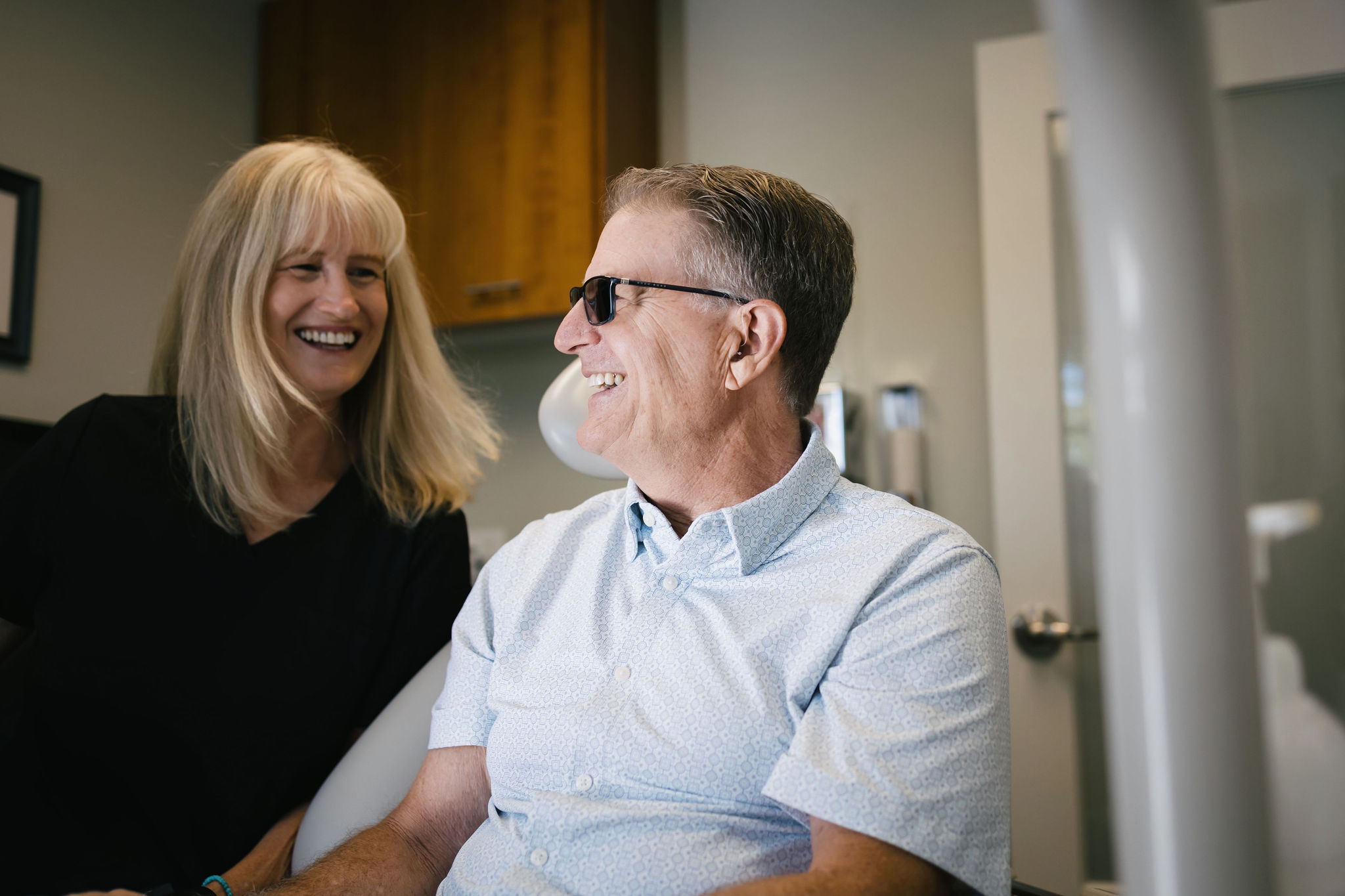 A patient is sitting in a dental chair and smiling at the dental hygienist because he is happy with his smile.