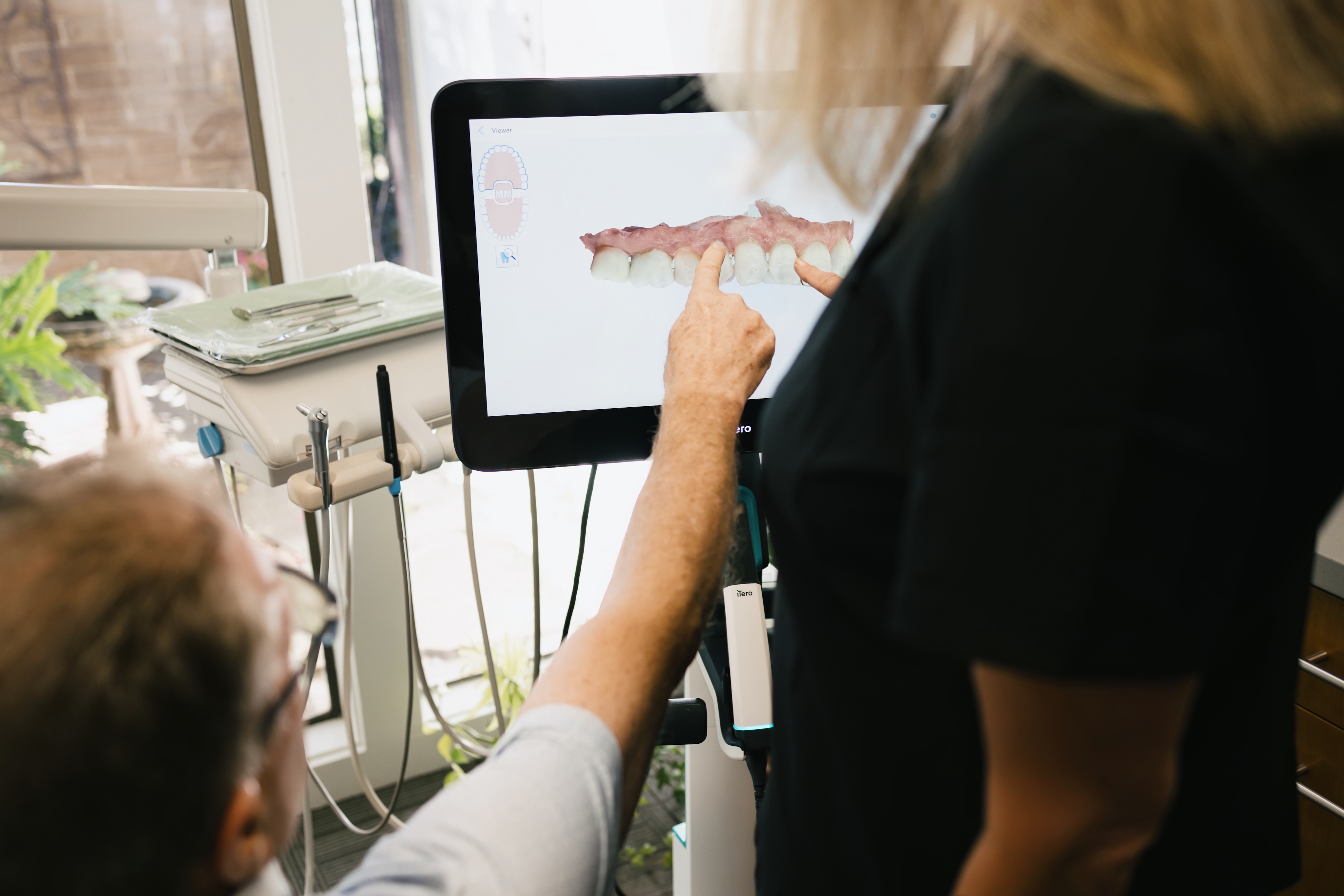 The dental patient and dental hygienist are both looking at a 3D rendering of the patients smile on the computer and talking about what his options are.