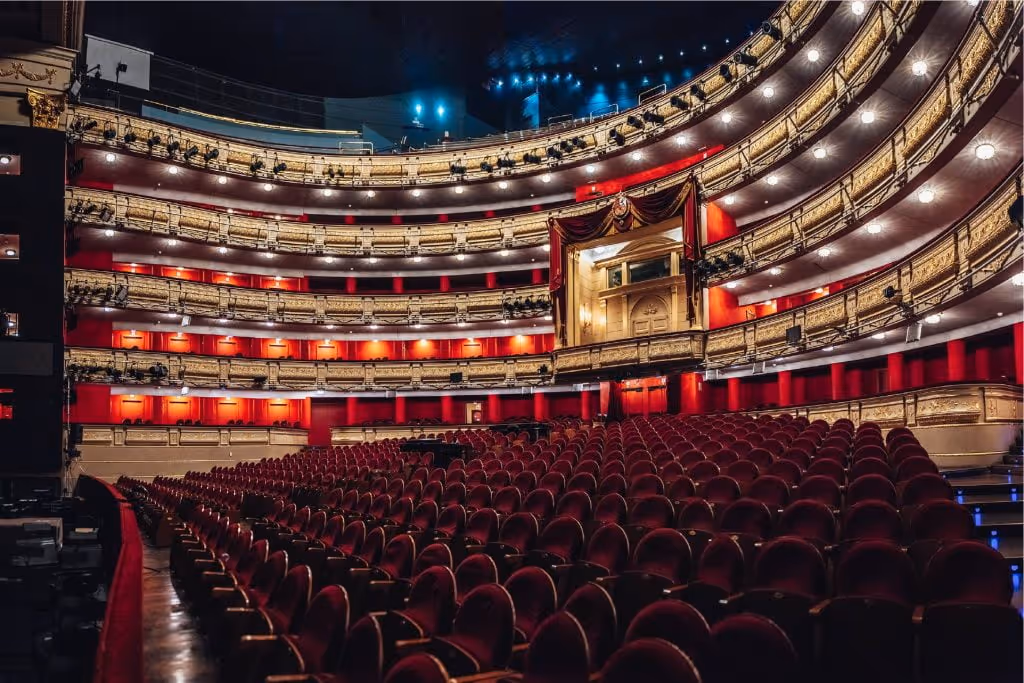 Interior del teatro Real, se ven múltiples balcones dorados y butacas rojas alineadas.