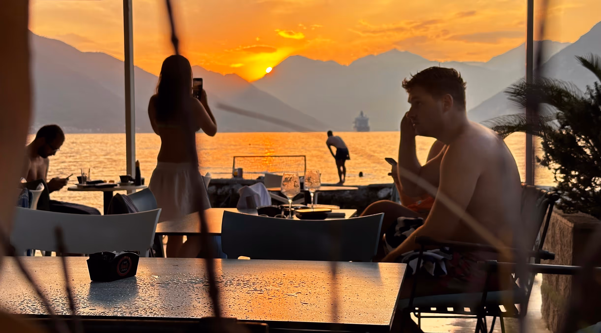 Waterfront dining at sunset with Bay of Kotor mountains, paddleboarder, and golden hour light in Montenegro