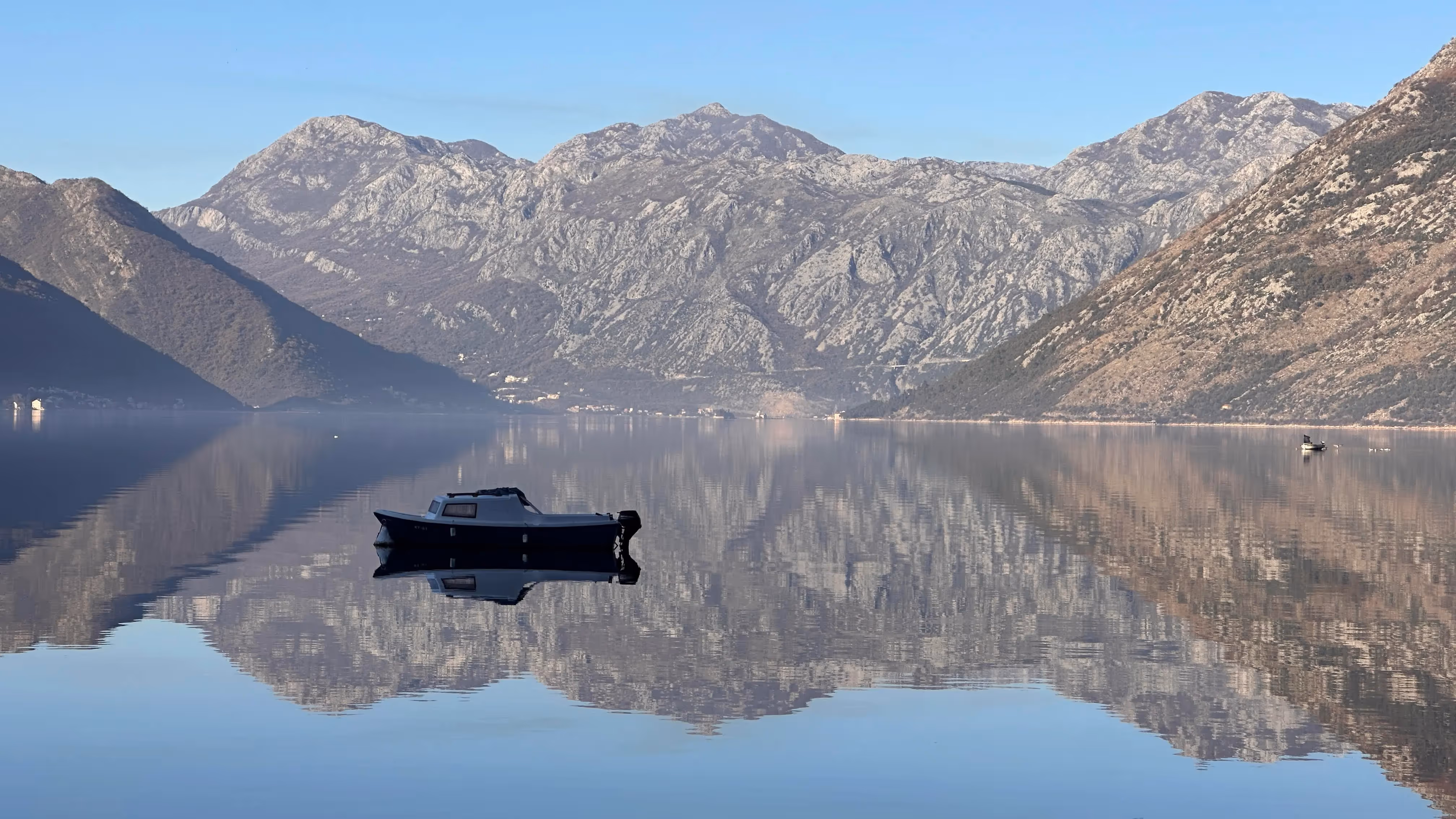 A small fishing boat on the mirror-flat waters of Kotor Bay, Montenegro, mountains reflected in the surface