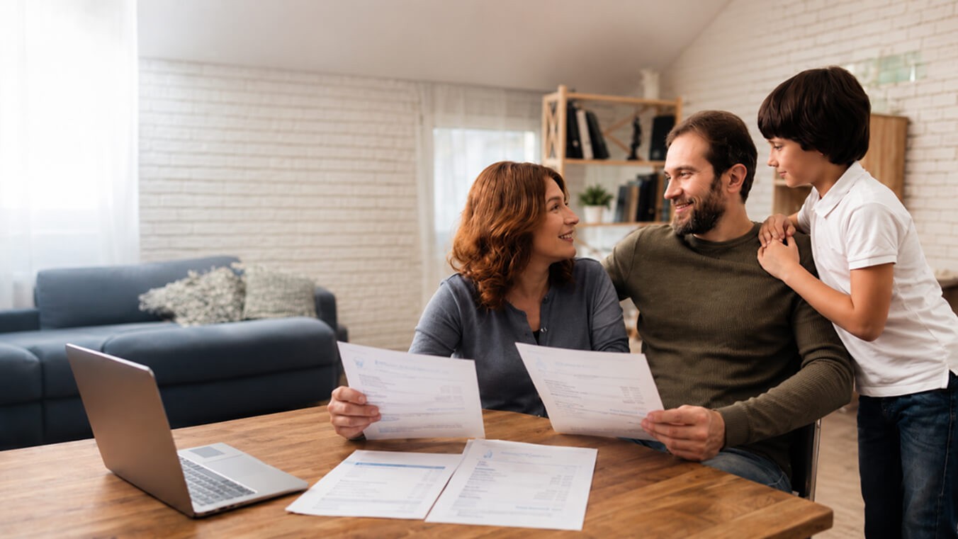 Veteran family seated at a dining table in a bright home, reviewing utility bills and paperwork together with a laptop nearby.