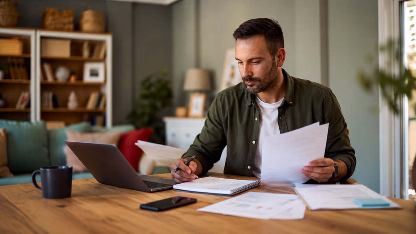 Young Australian veteran at home reviewing paperwork, taking notes, and using a laptop as he prepares for civilian employment and transition support after leaving the ADF.