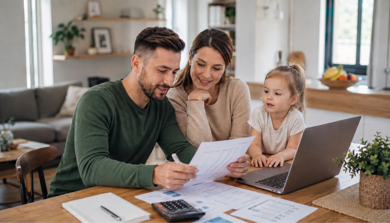 Young veteran family reviewing DVA payout documents at a kitchen table, with a laptop, calculator, and paperwork in a bright modern home.