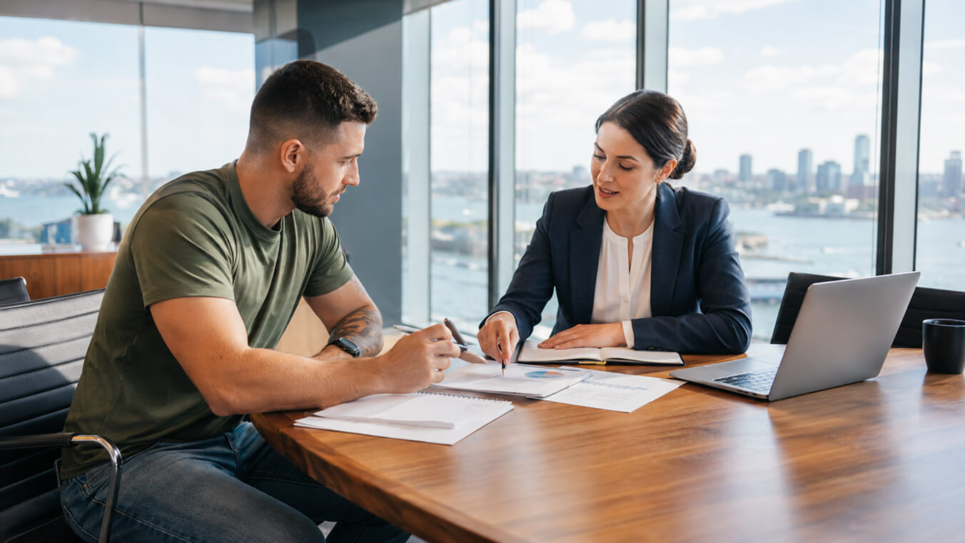 Young veteran reviewing business planning documents with a professional mentor in a modern office overlooking the city.
