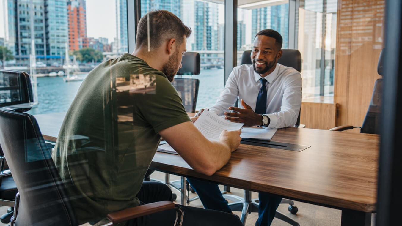 Male Australian veteran reviewing DVA compensation claim paperwork with a professional consultant in a modern office.