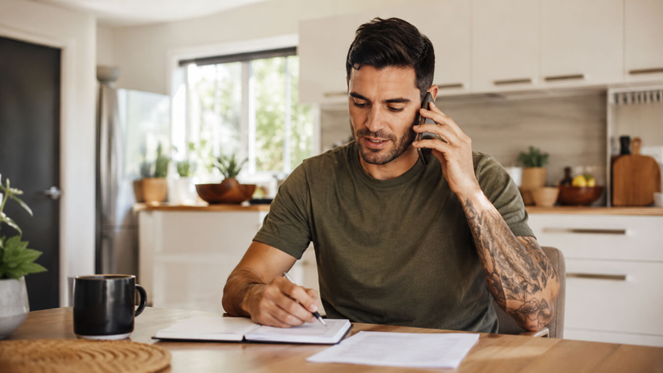 Young Australian veteran arranging a Veterans Home Care assessment by phone at his kitchen table.