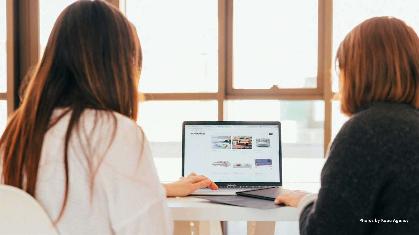 Two women facing away from camera and working on a laptop.