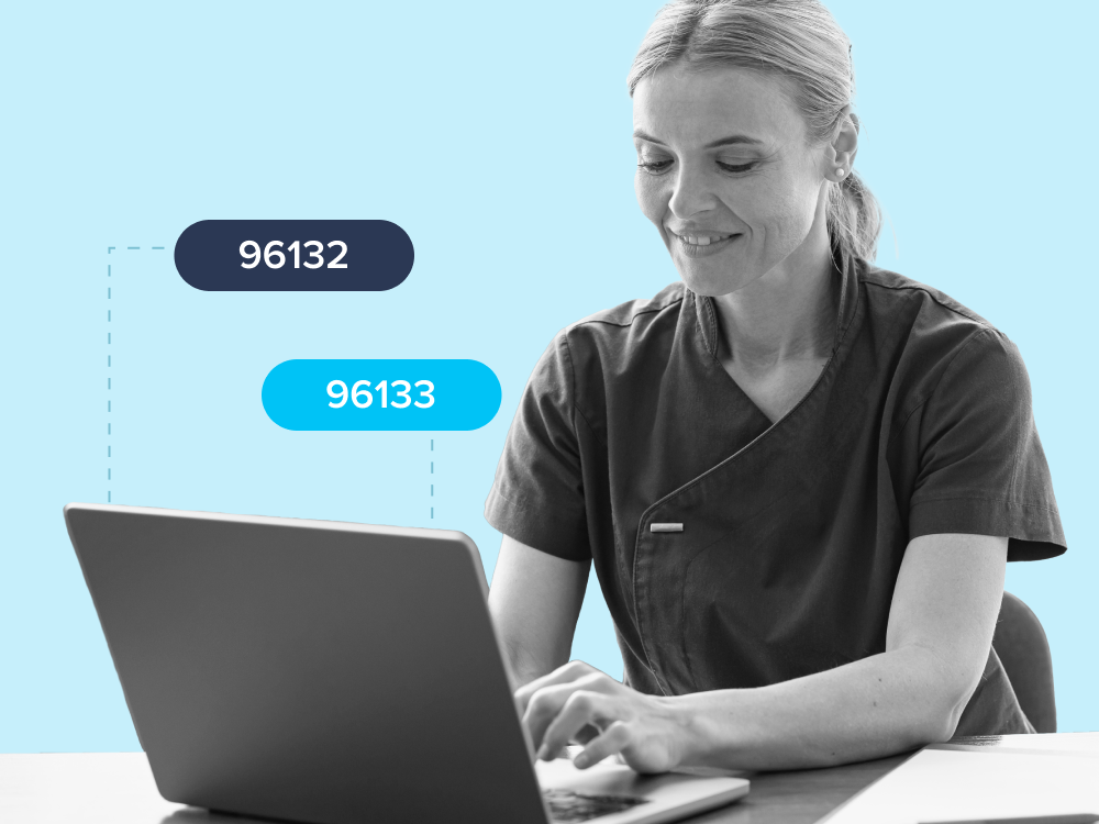 Smiling woman in medical scrubs typing on a laptop with codes 96132 and 96133 displayed nearby.