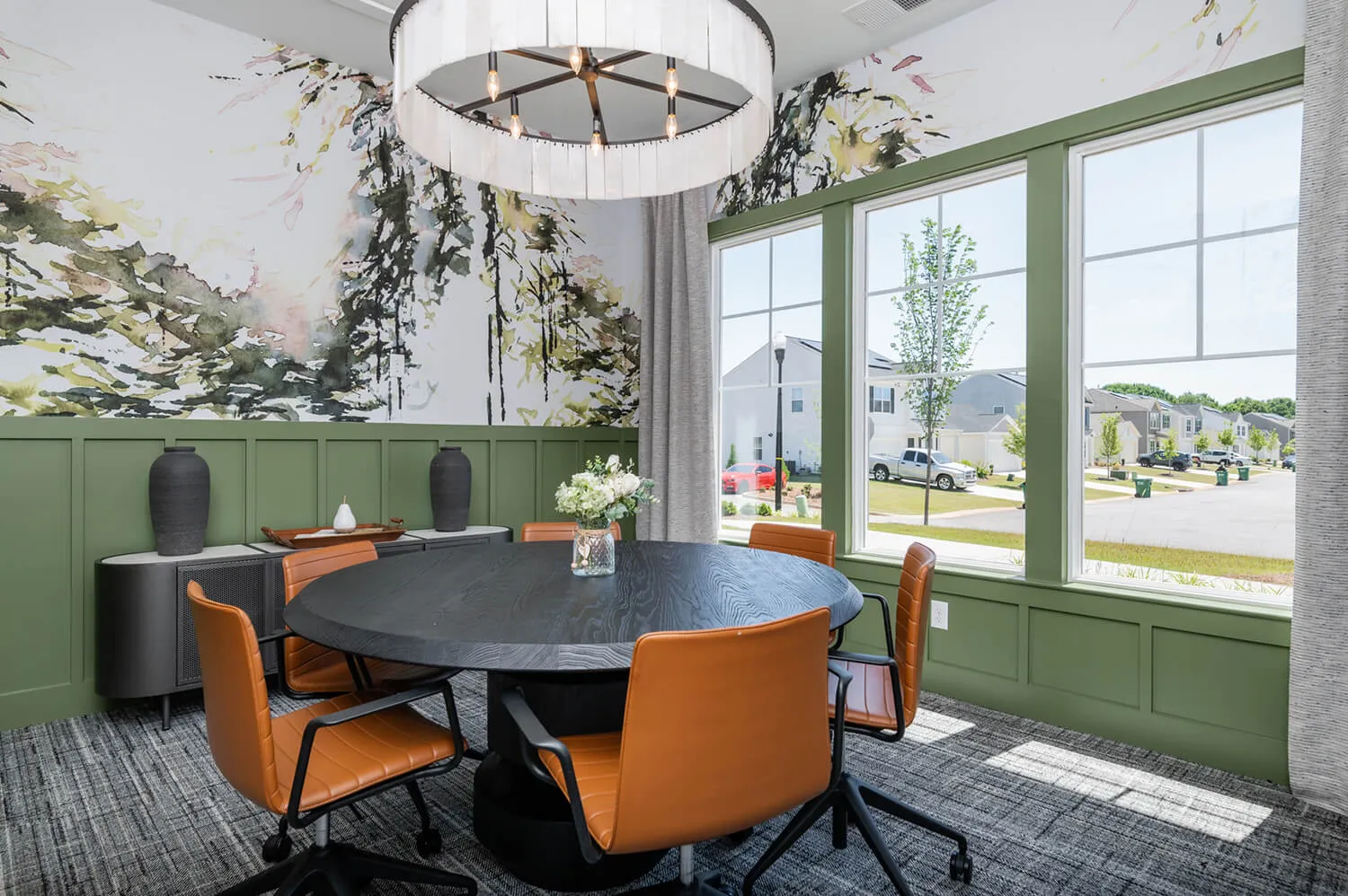 Modern conference room with round black table, orange chairs, green wainscoting, and large windows.