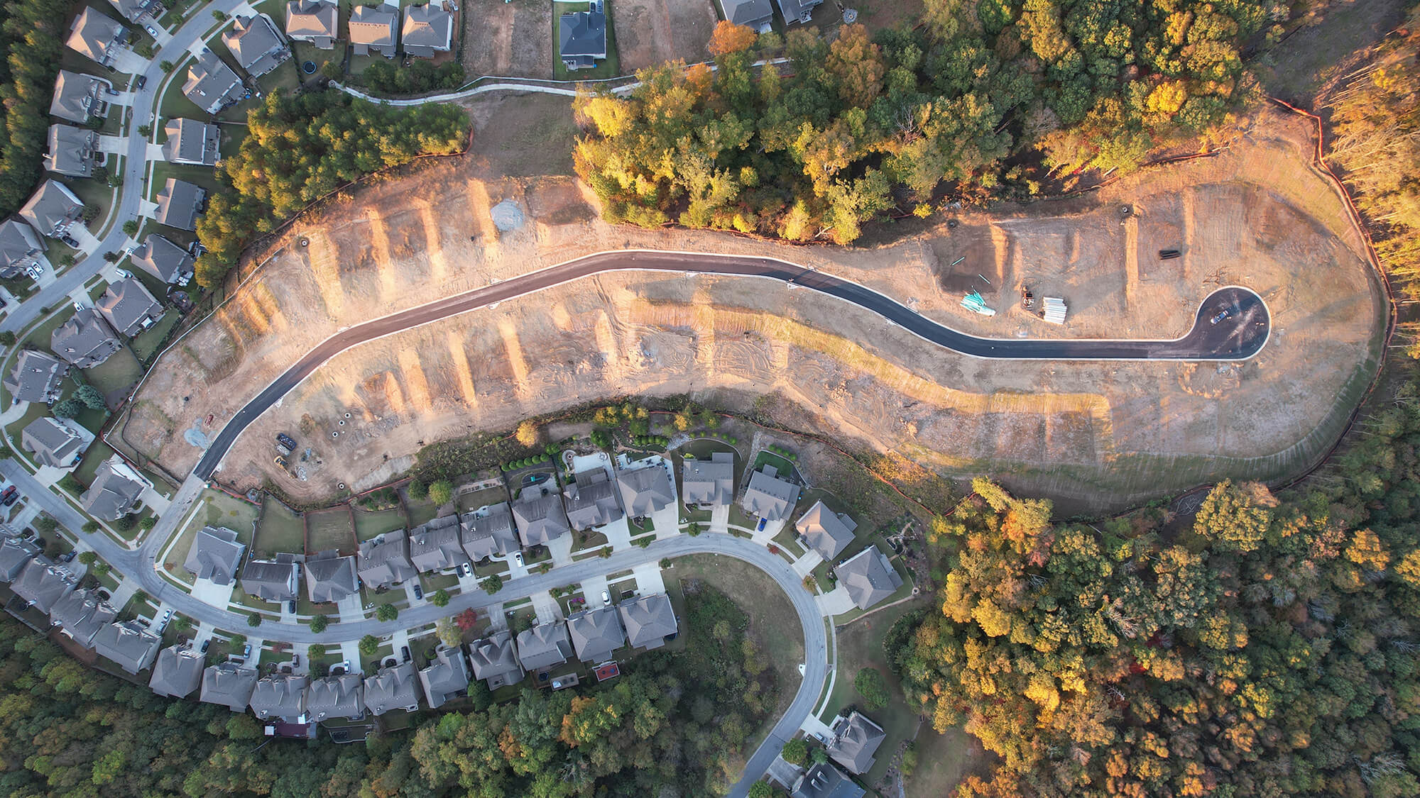 Aerial view of a residential neighborhood with a newly paved road and cleared lots for construction.