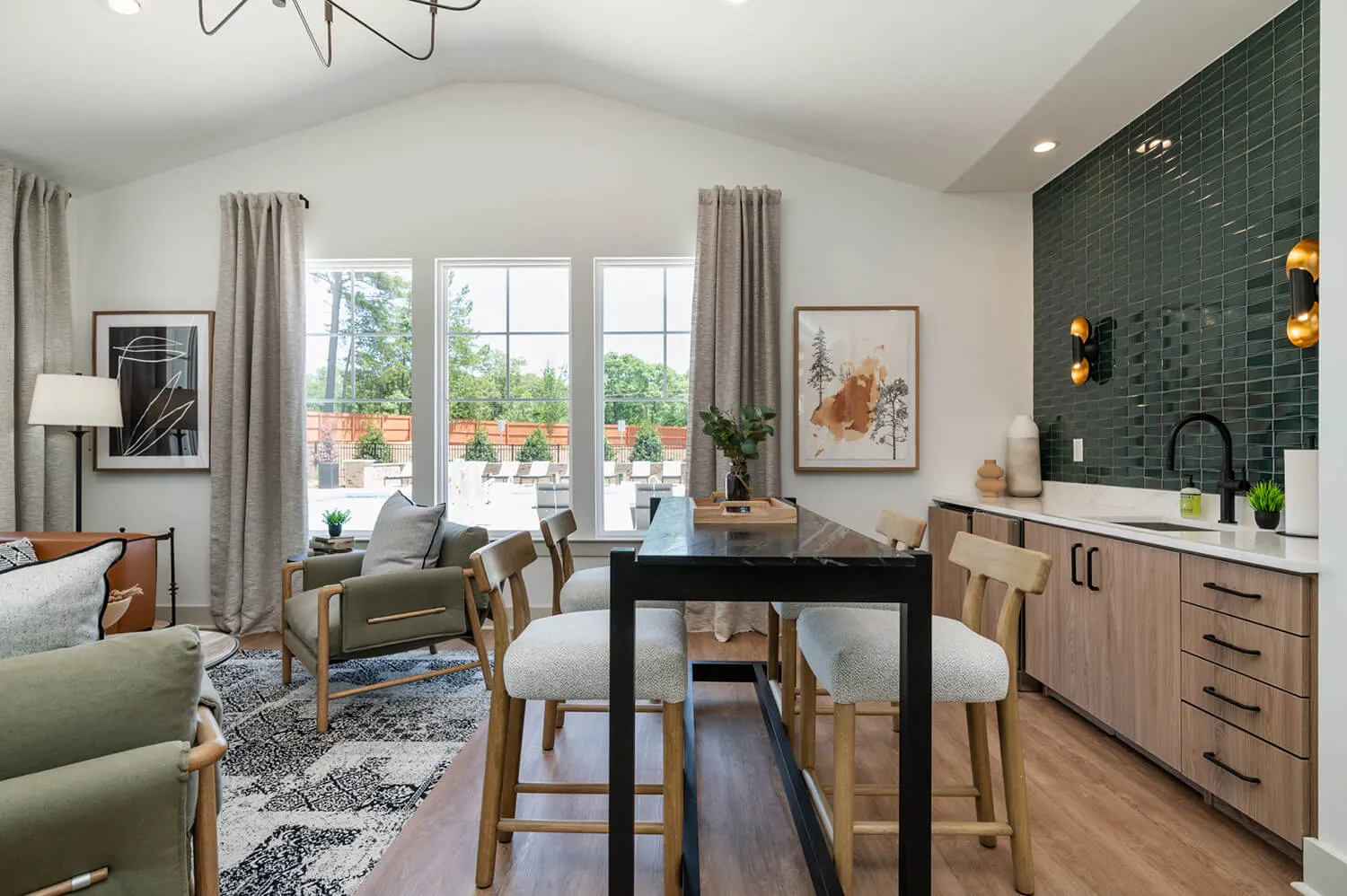 Modern dining and living area with black table, wooden chairs, green tiled wall, and large windows.