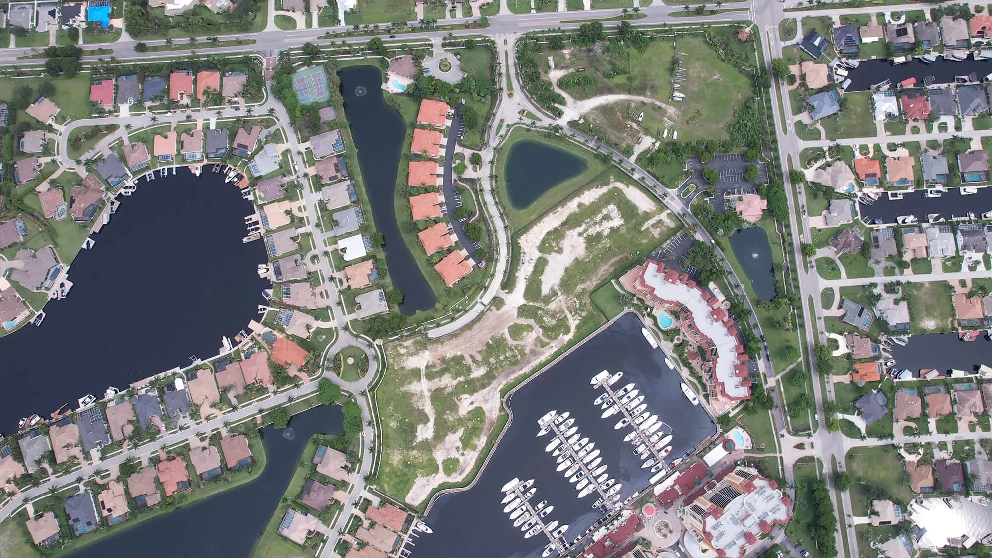Aerial view of a residential marina with houses, docks, boats, and roads around water bodies.