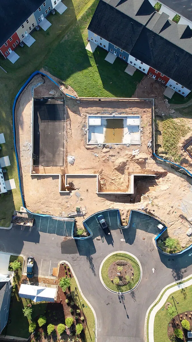 Aerial view of a construction site with foundation work near residential buildings and a roundabout.