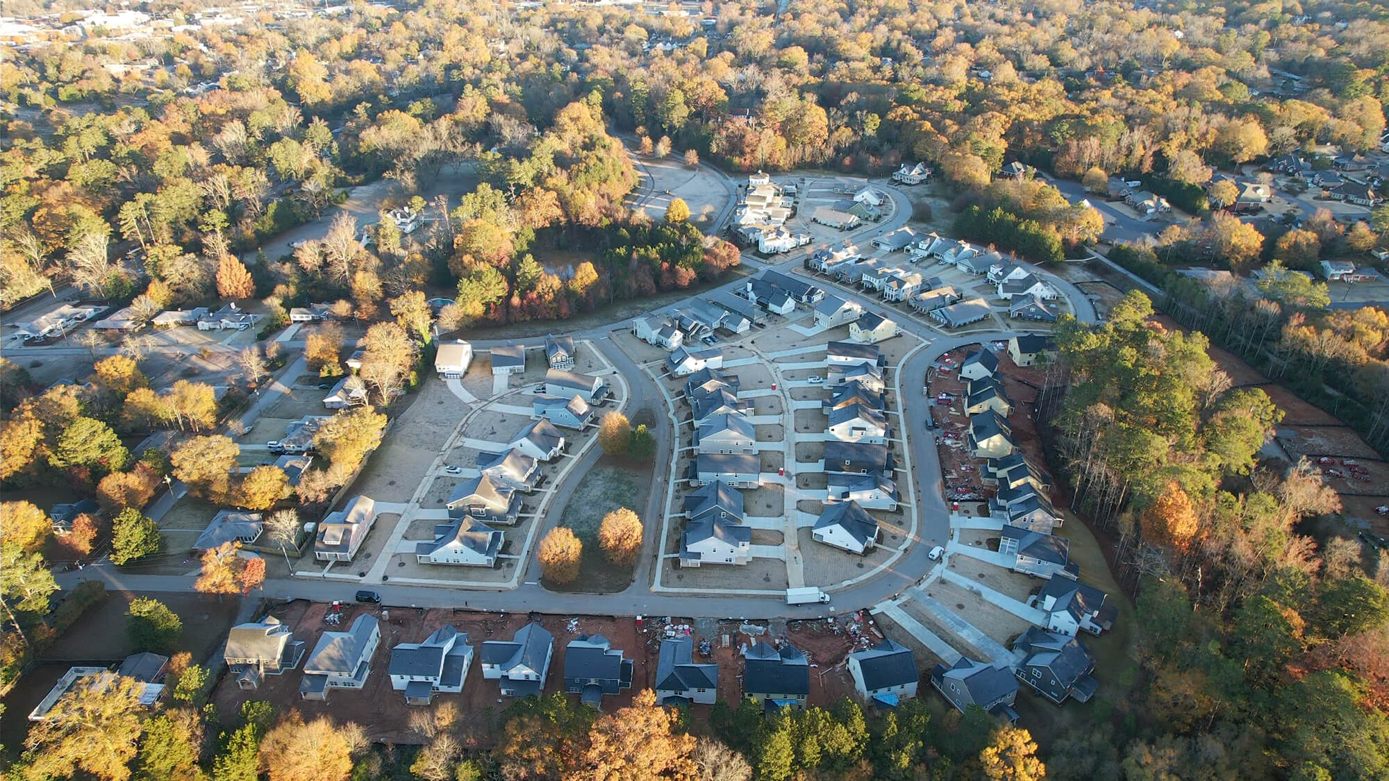 Aerial view of a suburban neighborhood with houses, trees, and winding roads in autumn.
