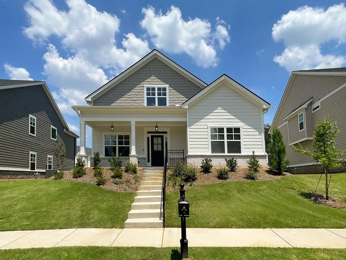 Modern single-story house with front porch, black door, steps, green lawn, and mailbox.