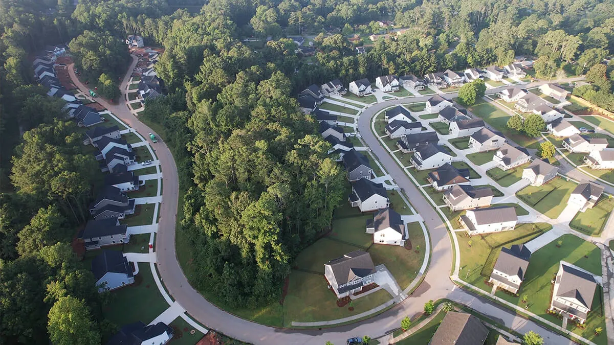 Aerial view of a suburban neighborhood with houses, curved roads, and a forested area in the center.
