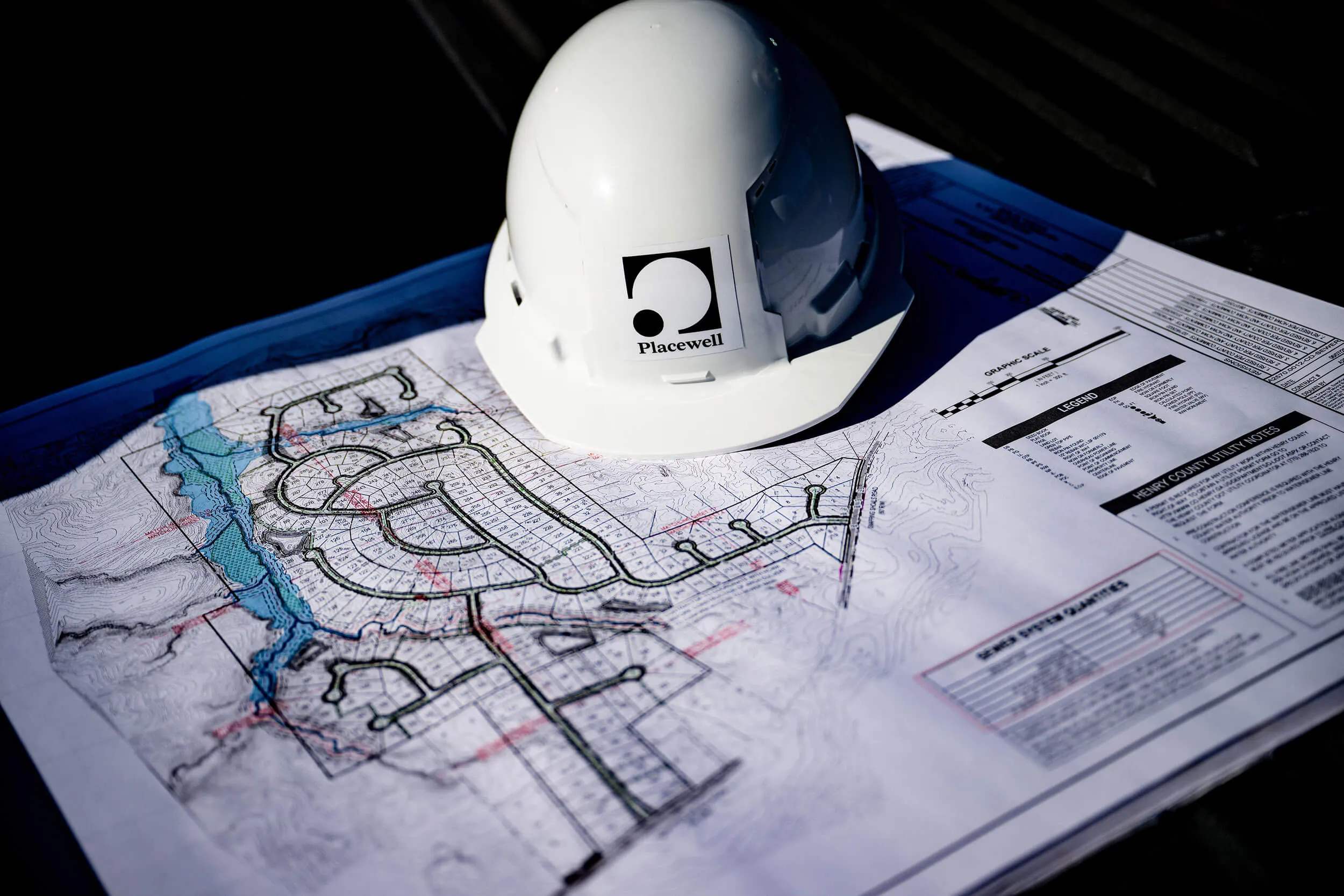 Construction helmet with Placewell logo resting on a detailed site development plan with roads and plots.