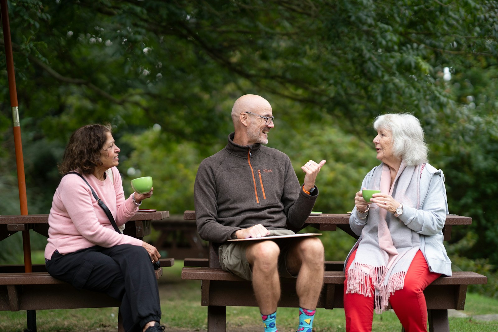 Three older adults sitting together on a park bench, talking