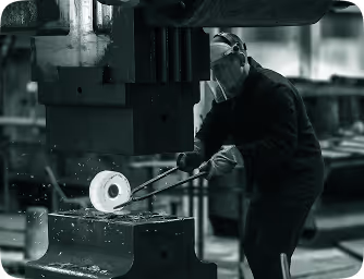 Worker wearing protective gear using tongs to handle molten metal in an industrial setting.
