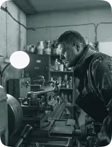 Man wearing safety glasses and apron operating a metal lathe in a workshop.