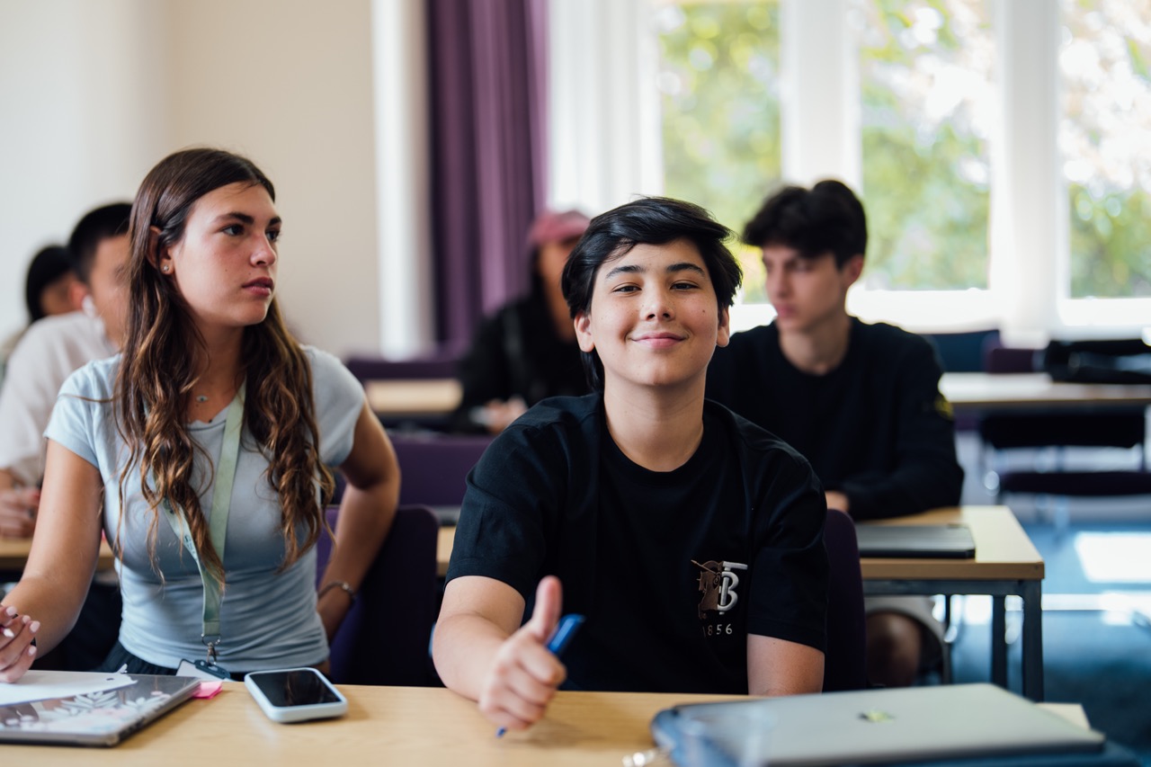 Teenagers participating in a classroom session at Oxbridge Summer Scholars, working at desks with notebooks and pens.